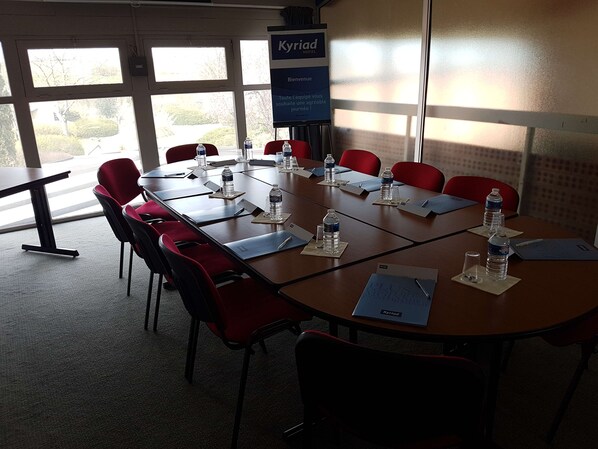 A conference room with a large table, red chairs, water bottles, and a sign for 'Kyriad Hotel'. - Kyriad Angoulême Nord Champniers - Hôtel & Résidence (Champniers)