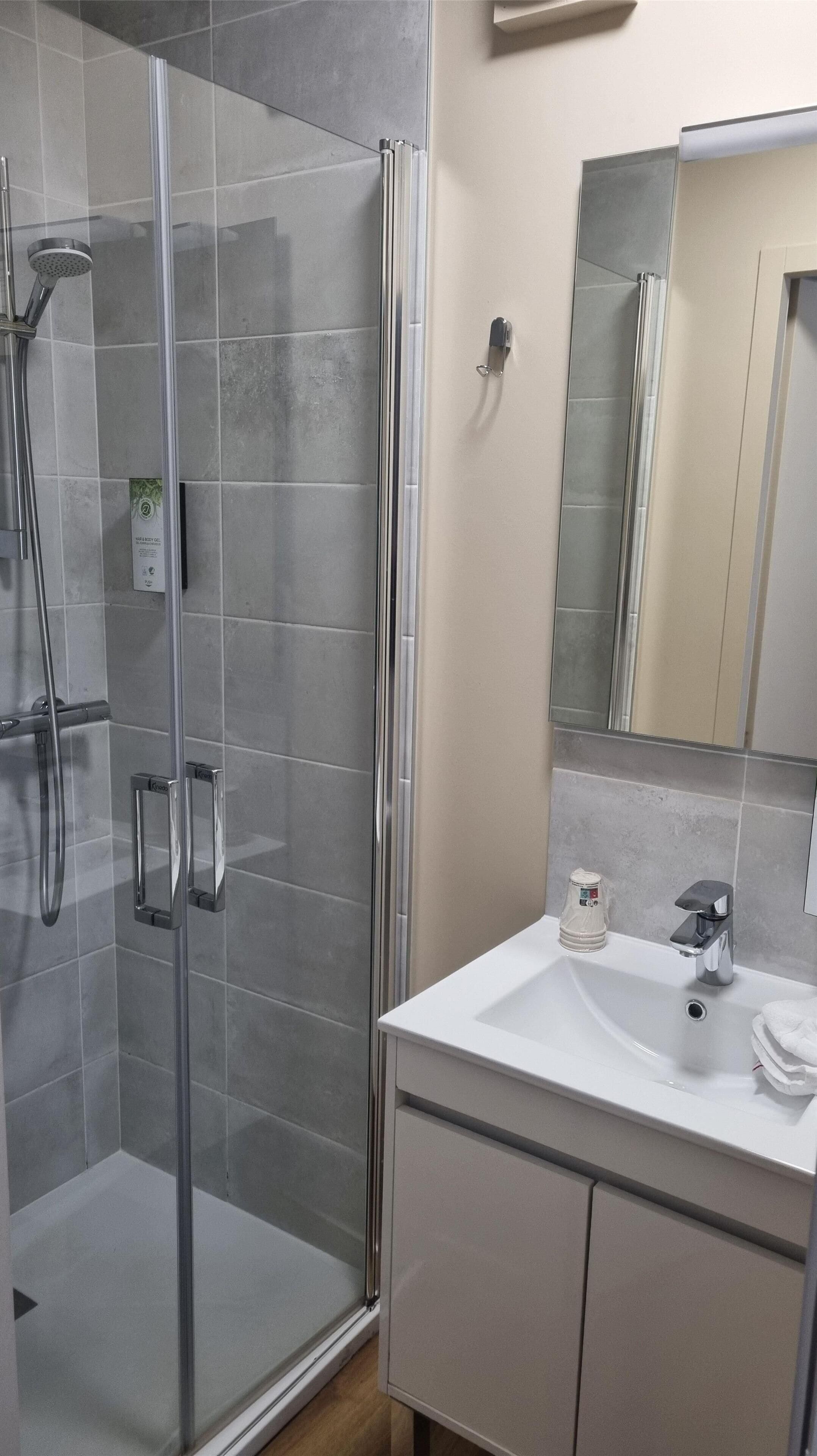 Ein modernes Badezimmer mit einer Glaskabine zur Dusche, einem weißen Waschbecken und einem Spiegel darüber.
