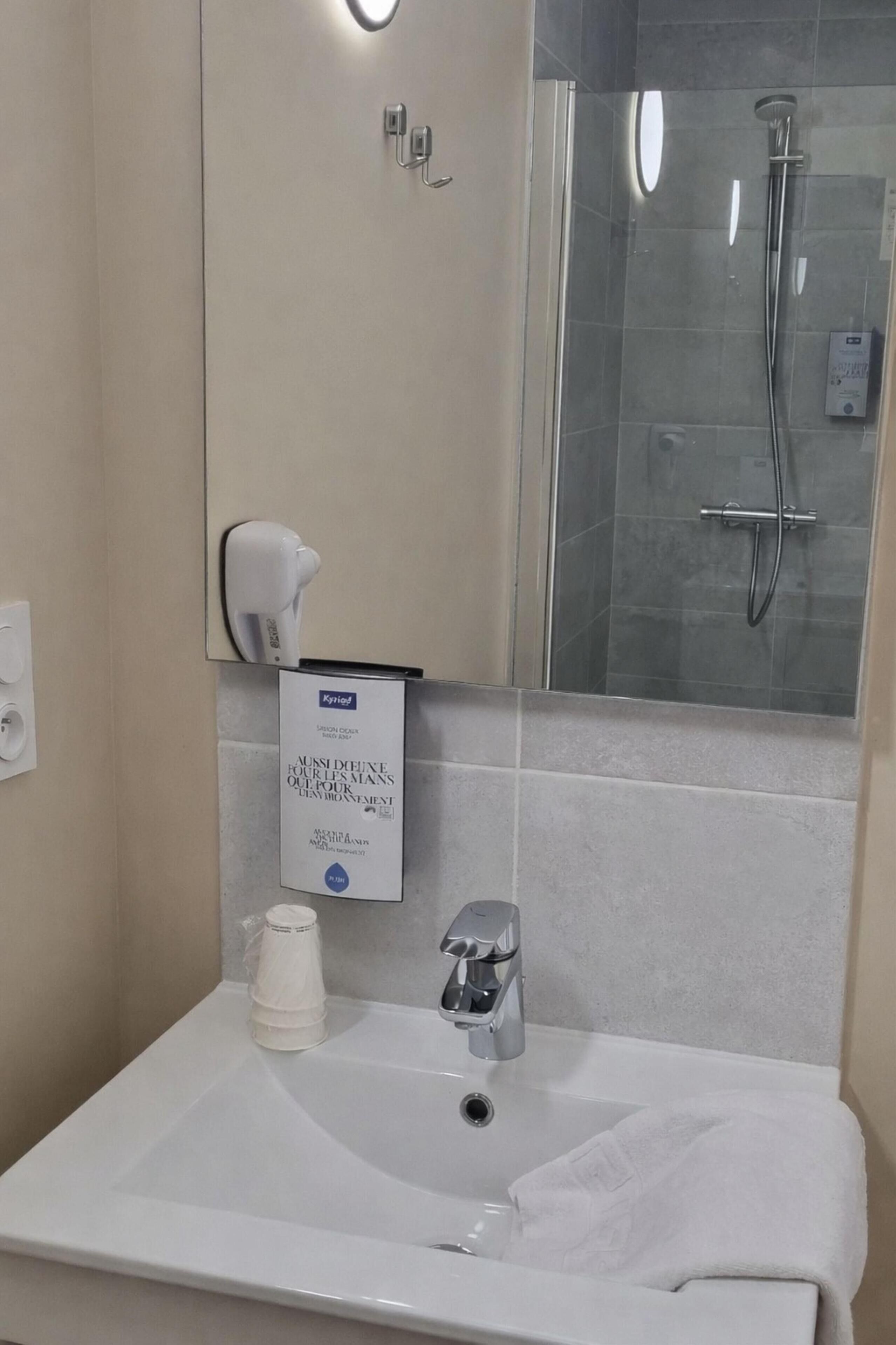 A bathroom with a white sink, a mirror, a glass shower enclosure, and a hand dryer.
