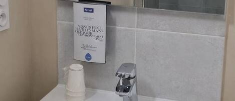 Un baño con un lavamanos blanco, un espejo, una cabina de ducha de vidrio y un secador de manos.