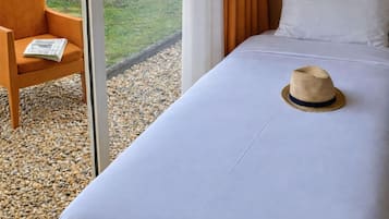 Een hotelkamer met een bed, een stoel, een hoed en uitzicht op een tuin.