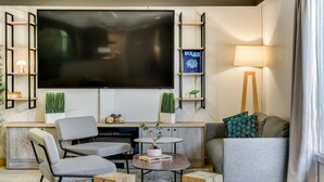 A modern living room with a flat-screen TV, comfortable seating, a coffee table, and a bookshelf. - Campanile NATURE - Bordeaux Ouest Le Bouscat (Le Bouscat)