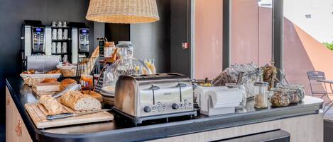 A breakfast bar with bread, a toaster, coffee machines, and various condiments.