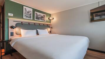 A hotel room with a large bed, a headboard with a circular light, and two framed pictures on the wall.