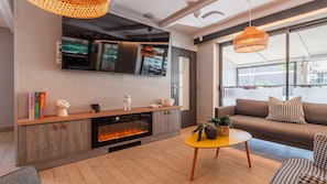 A modern living room with a fireplace, a sofa, a coffee table, and a television mounted on the wall. - Campanile NATURE - Colmar Parc des Exposition (Colmar)