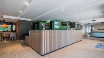A modern reception area with a green counter, wooden flooring, and a seating area with tables and chairs.