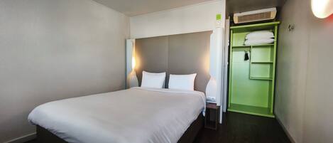 Una habitación de hotel con una cama, una mesita de noche, un armario verde y un aire acondicionado de pared.