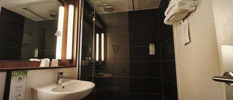 A modern bathroom with a white sink, a mirror, a glass shower enclosure, and a towel hanging on the wall.