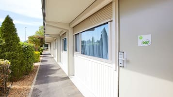 Ein Korridor mit weißer Außenwand, einer Tür mit einer Nummer und einem Fenster mit Jalousien.