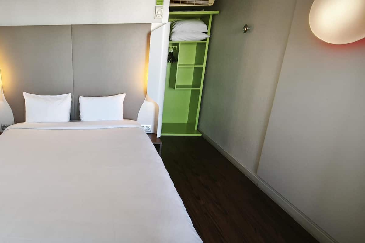 Une chambre d’hôtel avec un lit, des lampes de chevet, un meuble de rangement vert et une tête de lit blanche.