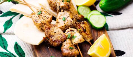 Skewers of grilled chicken on a wooden board with lemon wedges and cucumber slices.