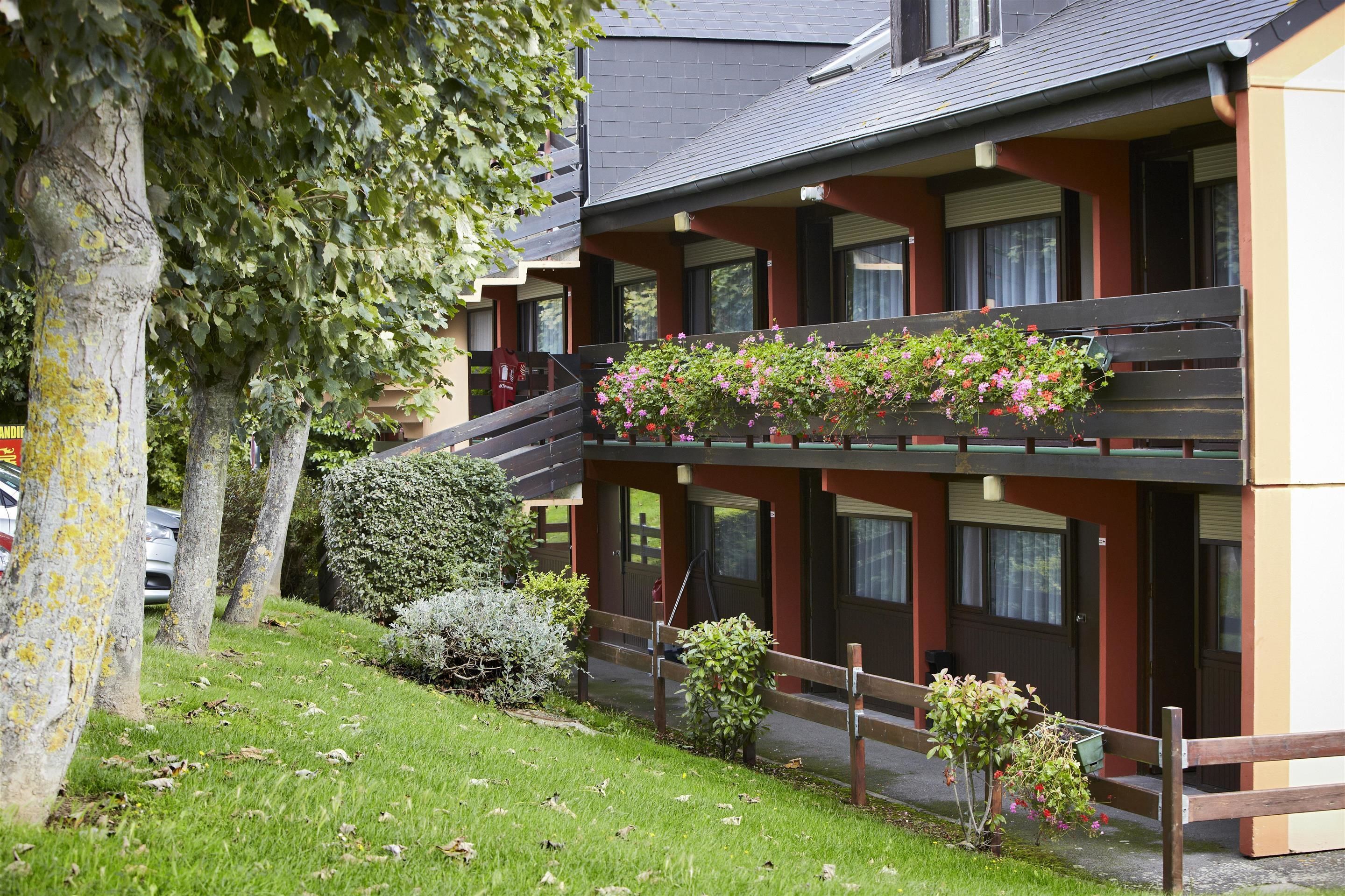 Un bâtiment à deux étages doté d’un balcon orné de fleurs, d’un petit jardin et d’une clôture en bois.