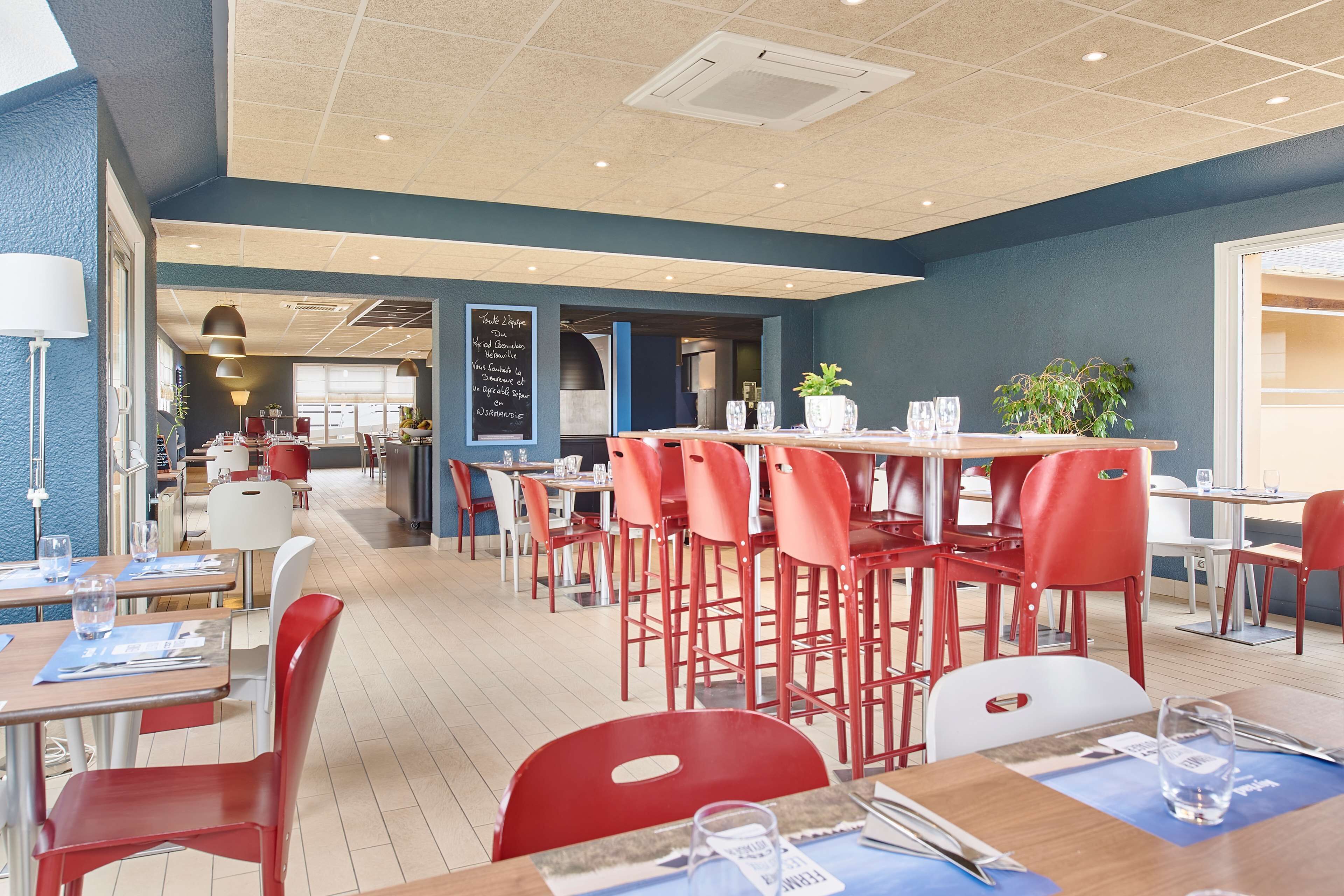 Un restaurante moderno con sillas rojas, mesas de madera y una pared azul como detalle.