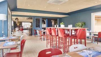 Un restaurante moderno con sillas rojas, mesas de madera y una pared azul como detalle.