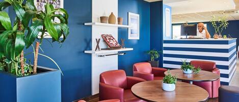 Un área de recepción con una decoración azul y blanca, sillas de cuero rojo, una mesa de madera con una planta y un mostrador de recepción con una computadora y un teléfono.