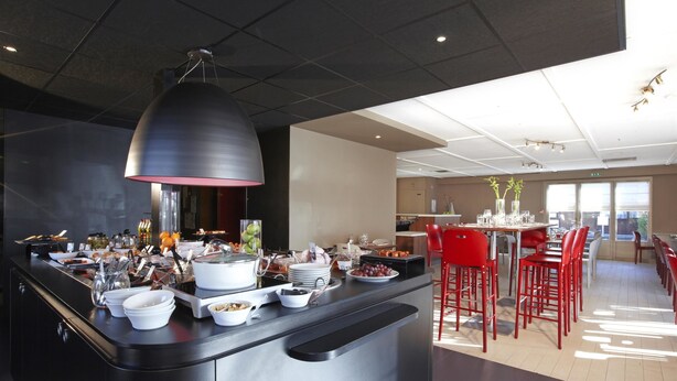 Un bar à petit-déjeuner moderne proposant une variété d’aliments et un espace détente avec des chaises rouges.
