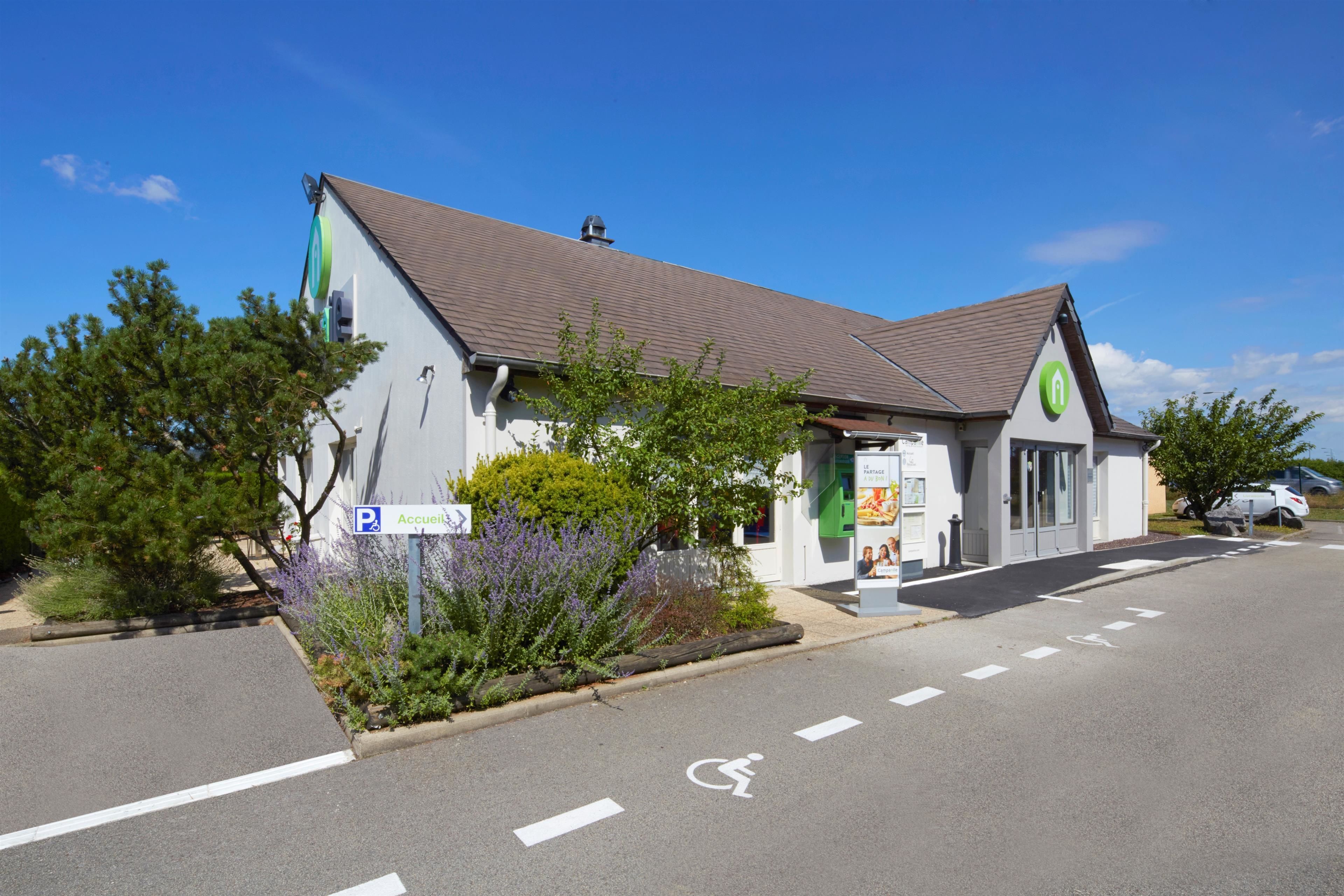 Un bâtiment avec un panneau indiquant un parking, un symbole d’accessibilité pour les personnes à mobilité réduite et un logo vert sur le toit.
