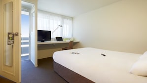 Une chambre d’hôtel avec un lit, un bureau avec un ordinateur portable, une télévision et une porte avec une pancarte.