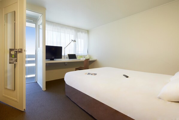 Een hotelkamer met een bed, een bureau met een laptop, een televisie en een deur met een bordje.