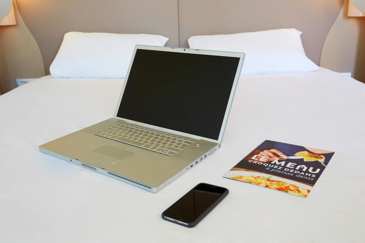Een laptop, een smartphone en een menukaart op een bed.