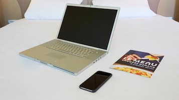 A laptop, a smartphone, and a menu brochure on a bed.