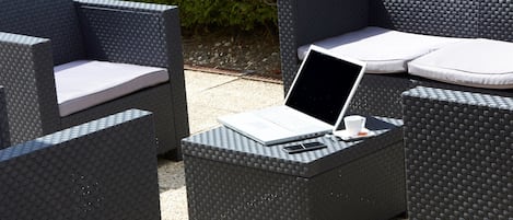 A wicker outdoor seating area with a laptop, a cup, and a smartphone on a small table.
