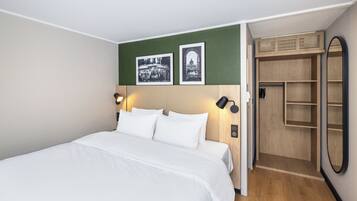 A hotel room with a bed, two wall-mounted lamps, a green accent wall, and a wooden wardrobe with a mirror.