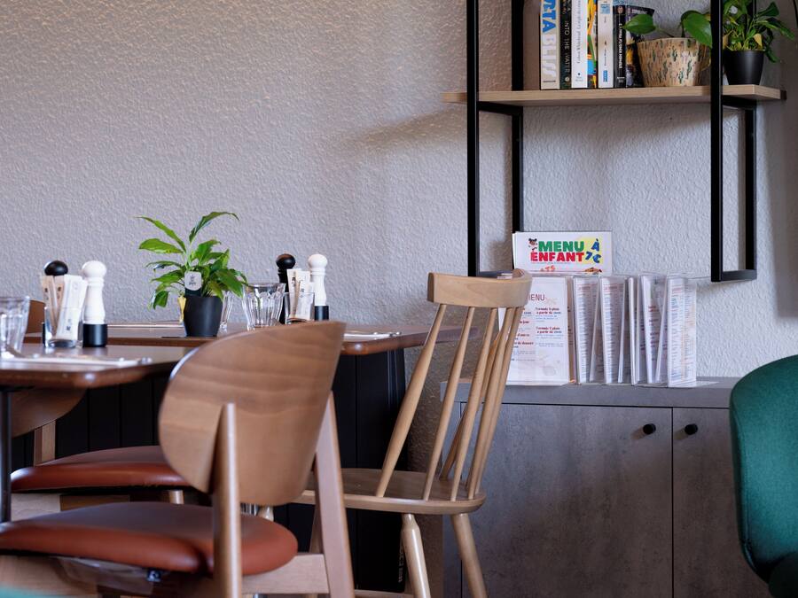A restaurant interior with a wooden table, chairs, potted plants, and a menu board.