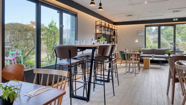 Un comedor moderno con mesas y sillas altas, un sofá y una estantería.