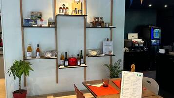 Interno di un ristorante con scaffali in legno che espongono prodotti alimentari, un espositore per il menu e una sala con tavoli e sedie.
