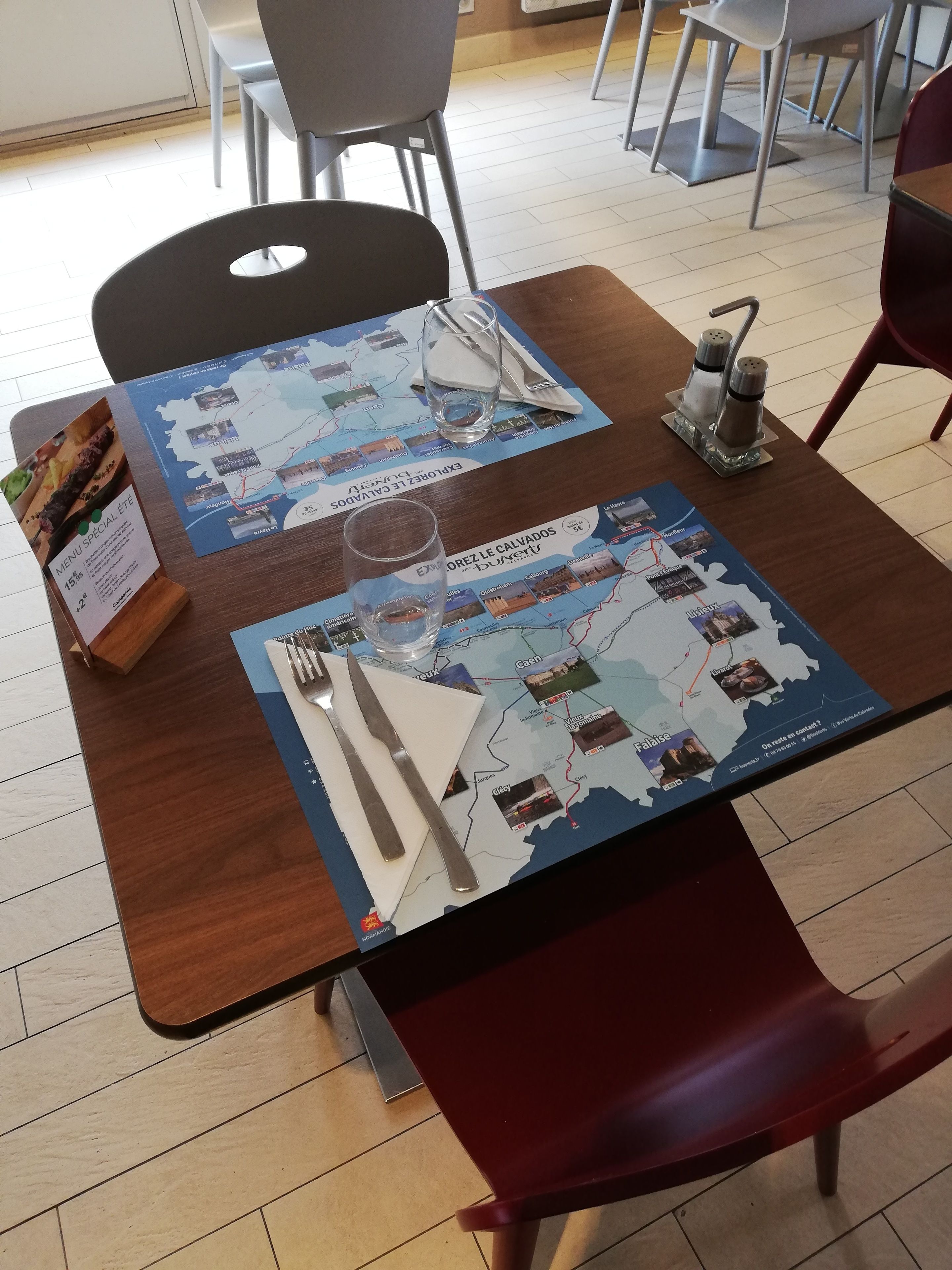 Een eettafel met een kaart van een regio, bestek, een glas en een menukaart.