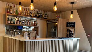 Zona de bar con mostrador de madera, focos colgantes y estanterías llenas de botellas de licores.