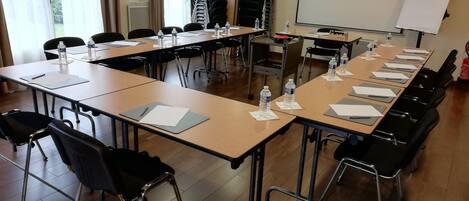 A conference room with long tables, chairs, water bottles, and a projector screen.