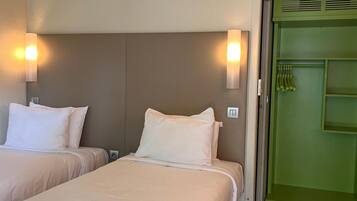 A hotel room with two beds, a green door, and a light switch on the wall.