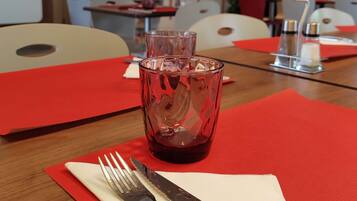 A dining table with a red placemat, a glass of red beverage, and cutlery.