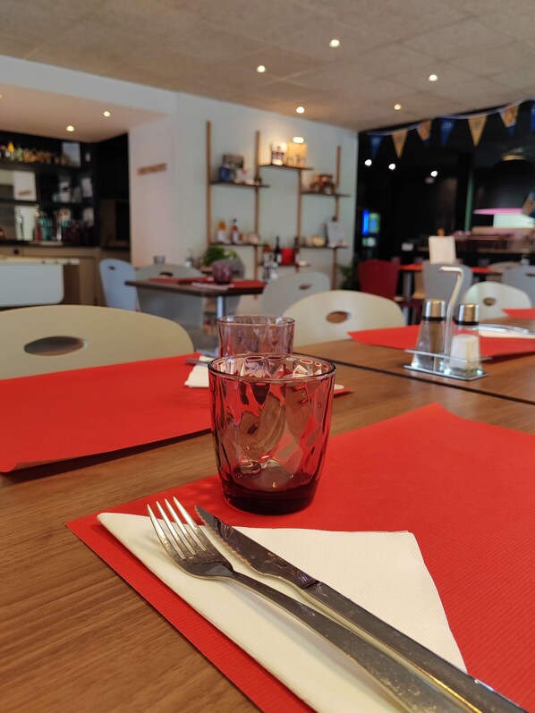 Una mesa de comedor con un mantelino rojo, un vaso de bebida roja y cubiertos.