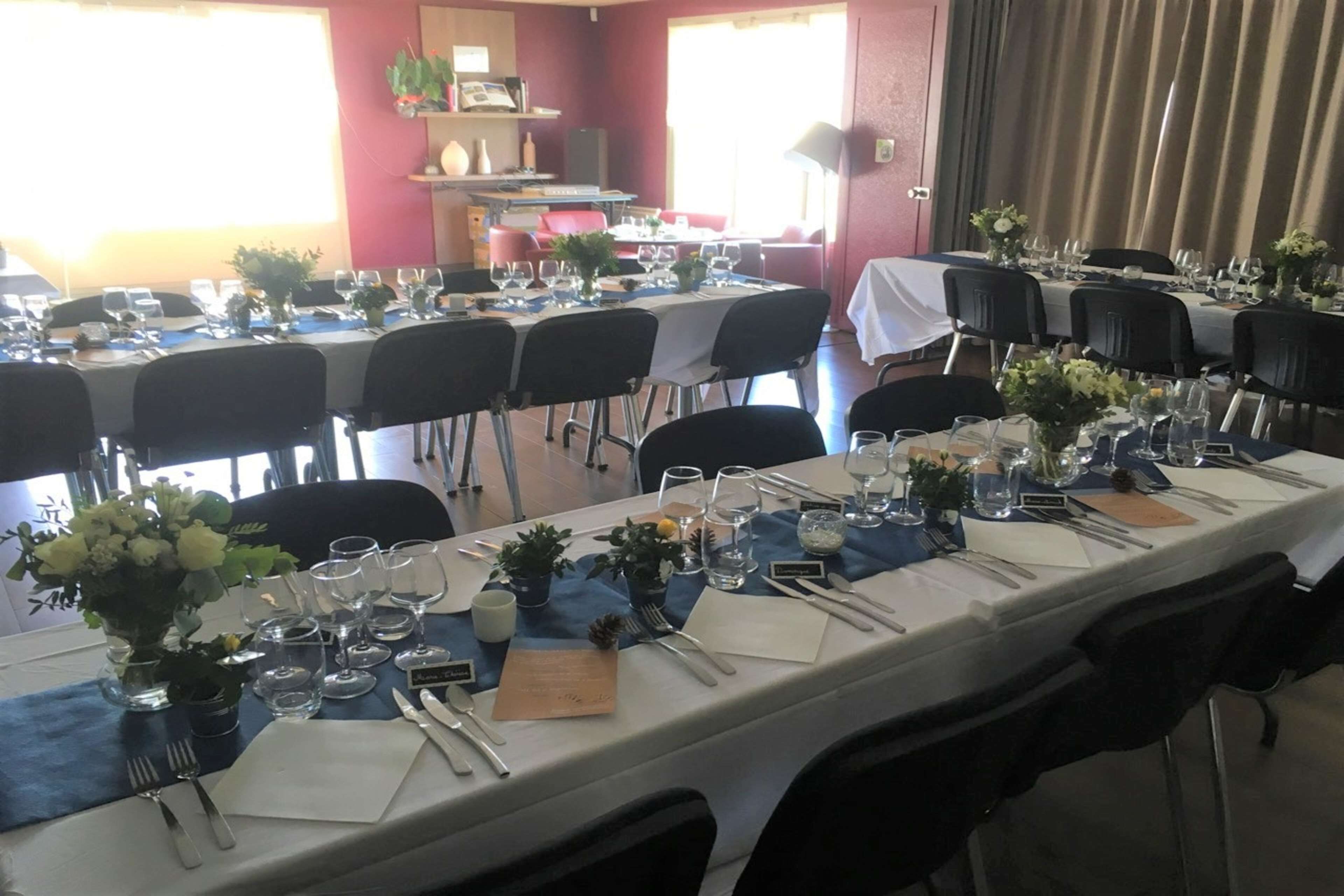 Comedor con varias mesas dispuestas para una comida, cada una con sillas, cubiertos y cristalería.