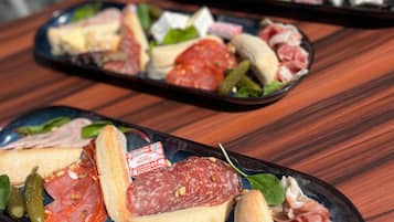 Una mesa con tres platos negros que contienen diferentes carnes, quesos y encurtidos.
