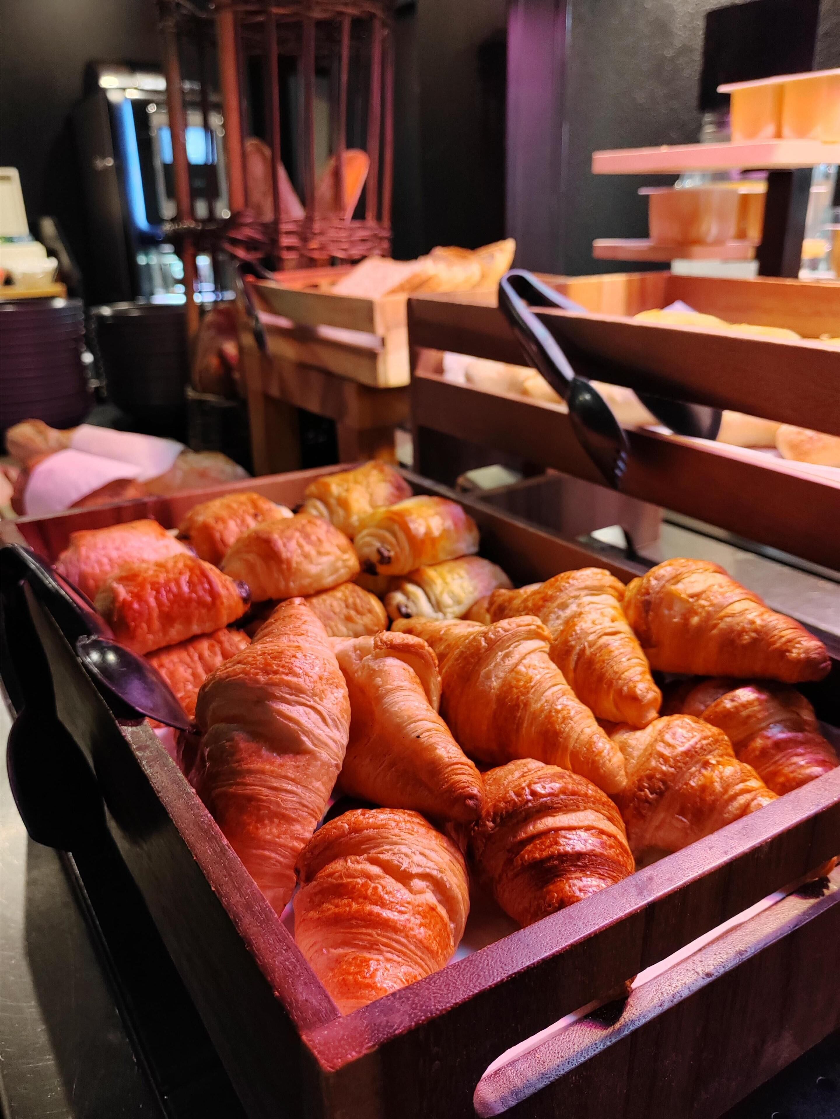 Eine Auswahl an Backwaren, darunter Croissants und andere Gebäcke, ansprechend auf Holztassen angerichtet.