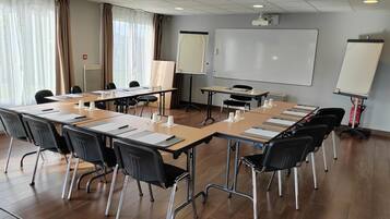 Un salón de conferencias con una larga mesa, sillas negras, una pizarra, un proyector y un extintor.