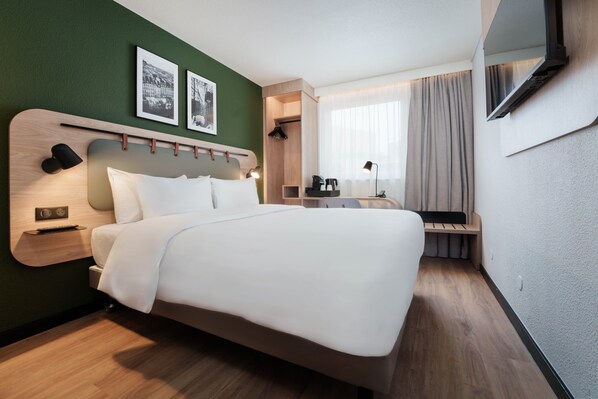 A modern hotel room with a large bed, a desk with a chair, a TV mounted on the wall, and a window with curtains. - Campanile PRIME - Dijon Centre Gare (Dijon)