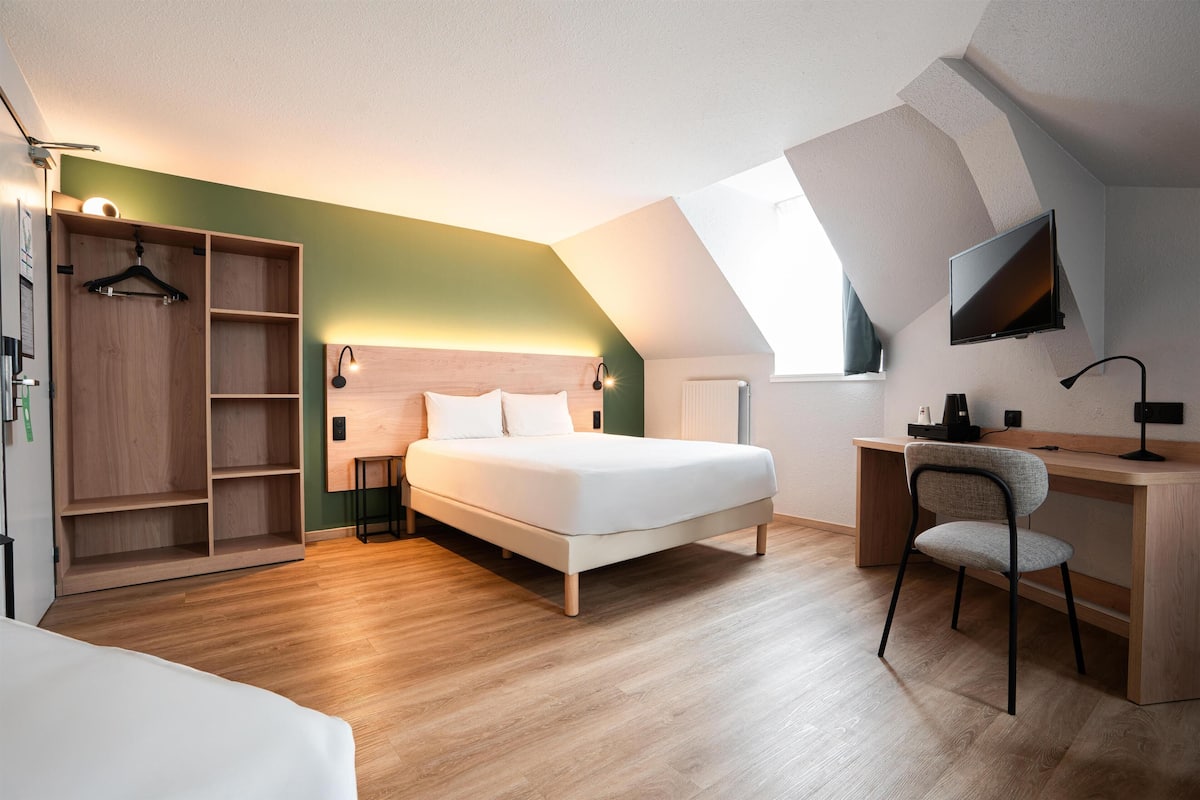 A bedroom with a bed, a desk, a chair, a wardrobe, and a TV.