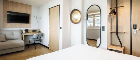 A modern hotel room with a bed, a desk, a sofa, a TV, a mirror, and a wardrobe.