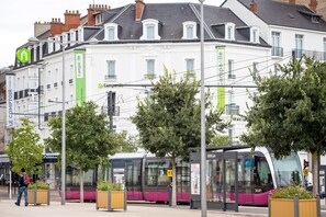 A tram station with a modern tram, a pedestrian, and a building with banners. - Campanile PRIME - Dijon Centre Gare (Dijon)