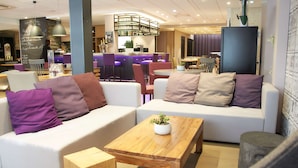 Un espacio lounge moderno con sofás, una mesa de centro de madera y una zona de bar al fondo.