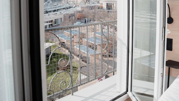 Un apartamento moderno con un amplio ventanal, vistas a un paisaje urbano y un balcón con barandilla de metal.