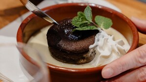 Un postre en un tazón con cuchara, una persona sosteniendo el tazón y una servilleta sobre la mesa.