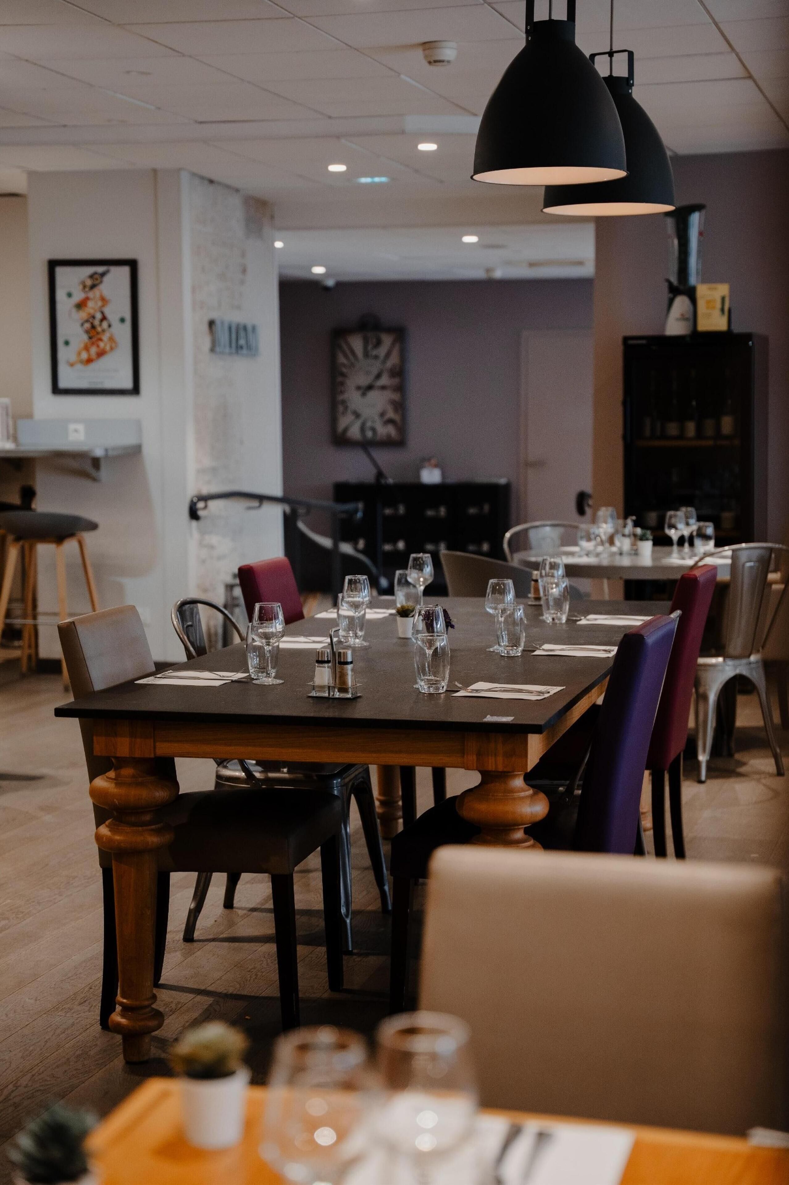 A restaurant with tables set for dining, a clock on the wall, and a bookshelf in the background.