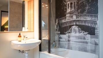 A bathroom with a sink, mirror, shower, and a wall mural of a bridge and fountain.