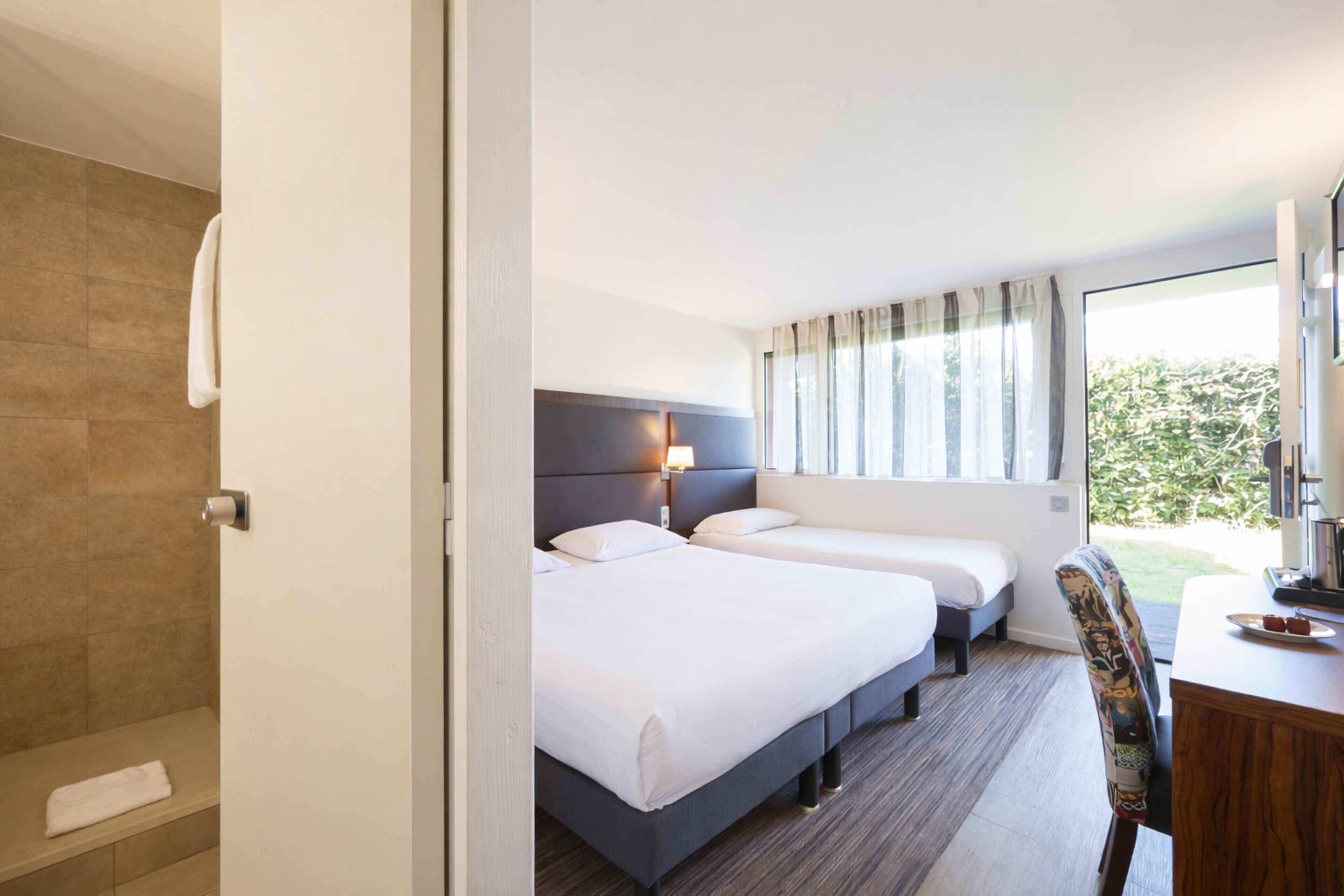 A hotel room with two beds, a shower, a desk, and a chair.